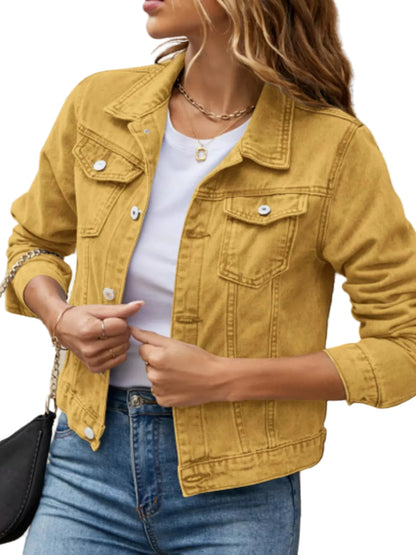 A woman wearing a mustard yellow denim jacket over a white t-shirt and blue jeans, standing against a textured stone wall.