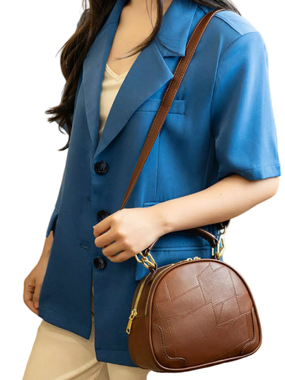 A woman wearing a blue short-sleeve blazer and cream pants carries a brown faux-leather crescent-shaped shoulder bag with a quilted pattern and gold hardware.