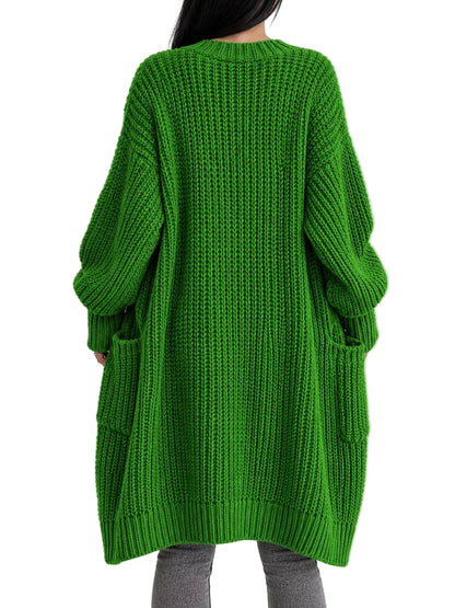 A person viewed from the back wearing an oversized bright green chunky knit sweater with long sleeves and side pockets, paired with gray pants, against a plain light background.