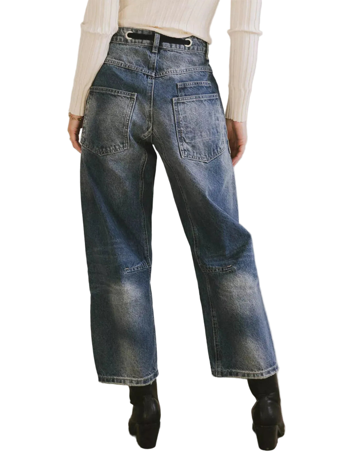 A person shown from the back wearing high-waisted wide-leg blue denim jeans with a cream ribbed sweater and black ankle boots, standing against a plain light wall.