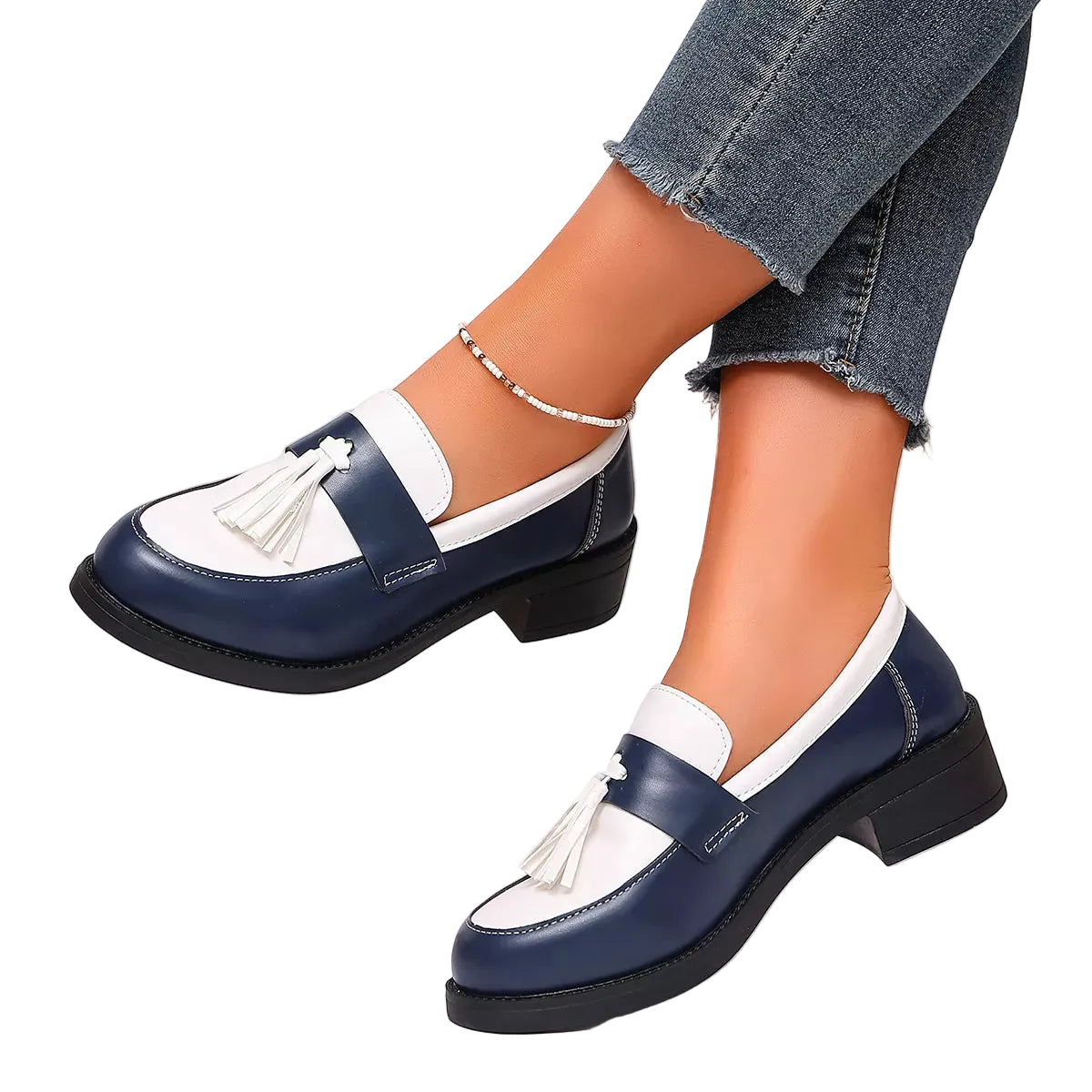 A pair of women's navy blue and white leather loafers with tassel details, shown on a model's feet wearing frayed blue jeans. The shoes feature low block heels and are photographed against a clean white background with a decorative pink rose in the corner.