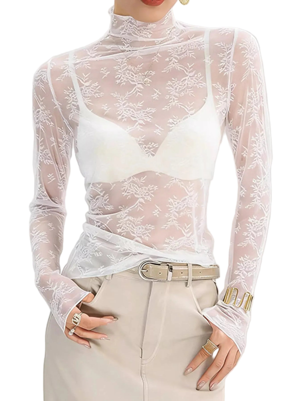 A woman wearing a sheer white floral lace long-sleeve mock-neck top over a white bralette, paired with beige trousers and a belt.