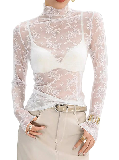 A woman wearing a sheer white floral lace long-sleeve mock-neck top over a white bralette, paired with beige trousers and a belt.