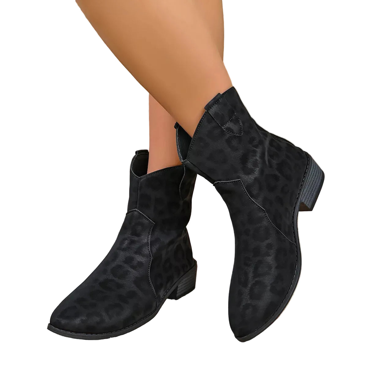 Black leopard-print ankle boots with low block heels, shown on a model's feet against a textured beige wall, with a brown hat resting nearby.