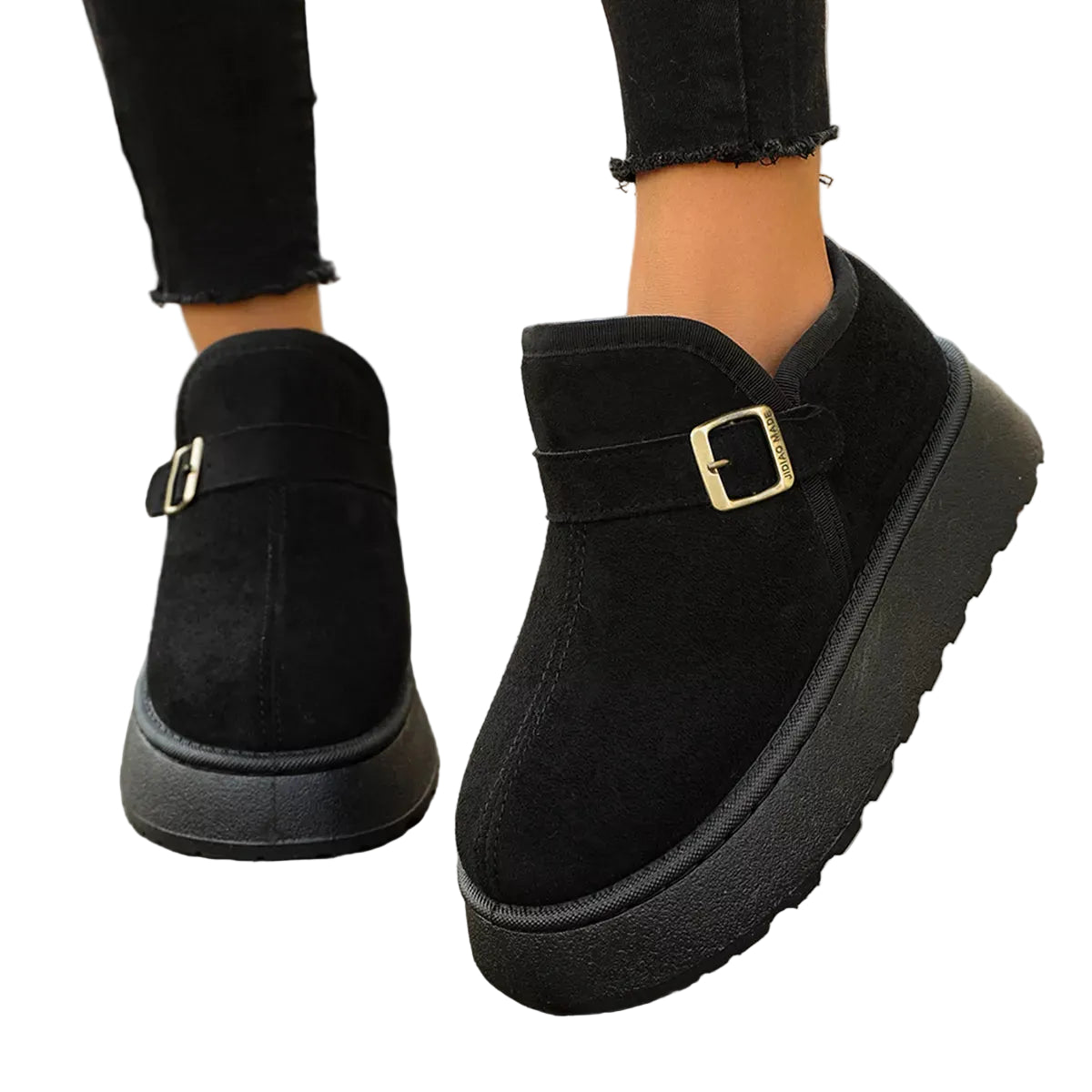 Black platform ankle boots with a buckle strap detail, shown on a person wearing black jeans on a wooden deck.