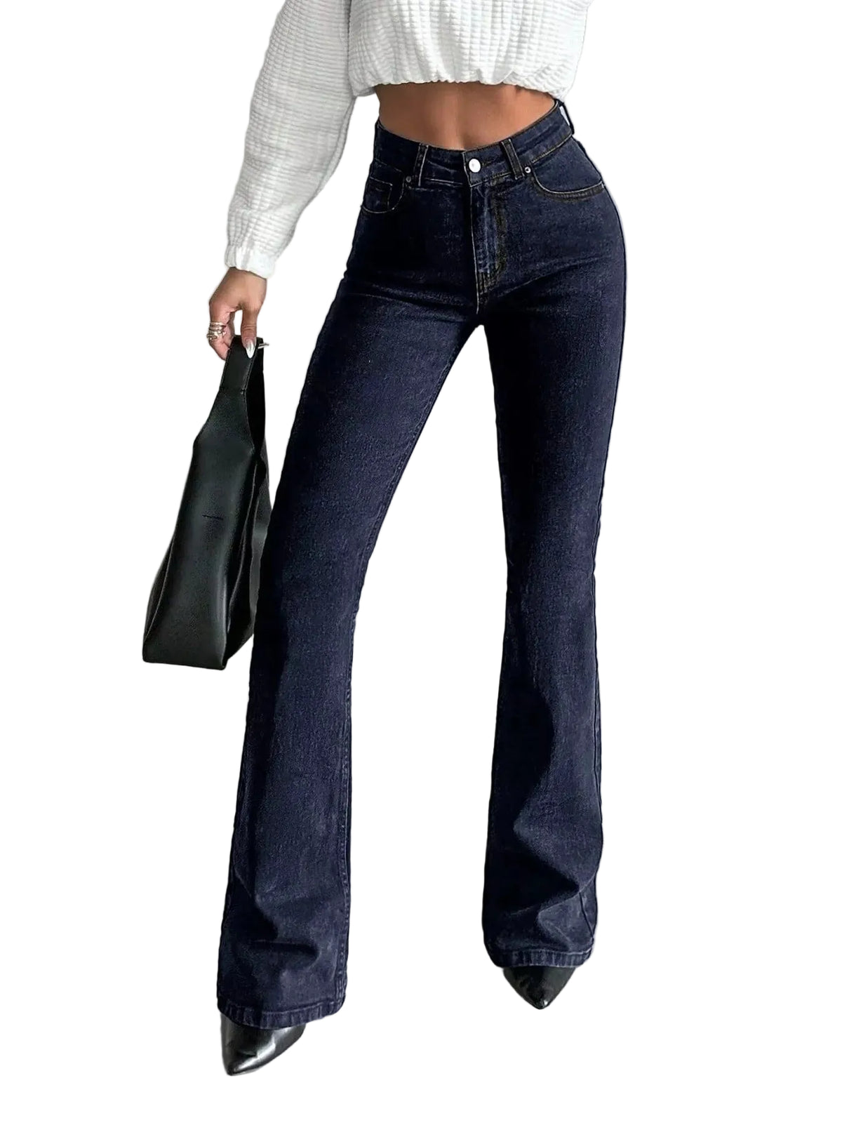 A person wearing dark blue high-waisted flare jeans with a white ribbed long-sleeve crop top and black pointed shoes, holding a black tote bag in a minimalist gray room.