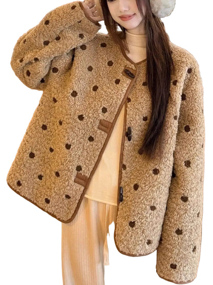 A woman wearing a beige sherpa fleece jacket with dark brown polka dots and brown trim, styled over a cream turtleneck and cream pants in an indoor setting.