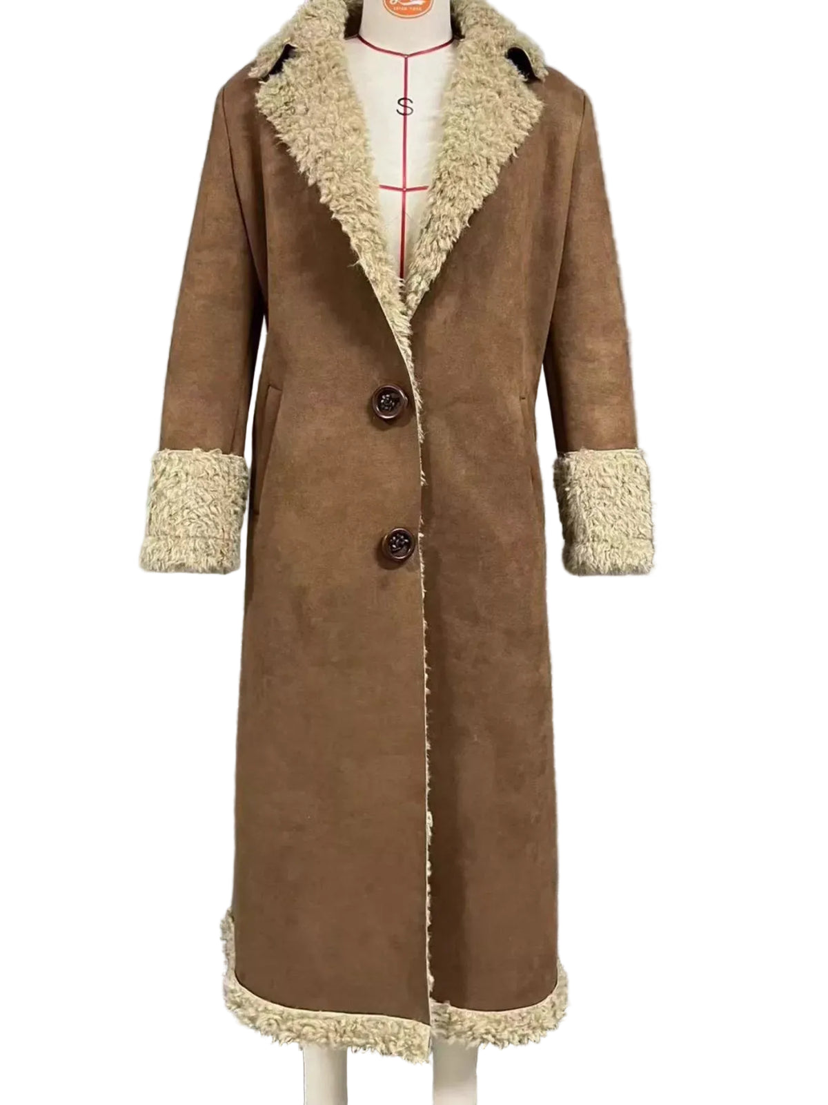 A long brown suede-like coat with cream shearling-style trim on the collar, cuffs, and hem, displayed on a mannequin in front of window blinds.