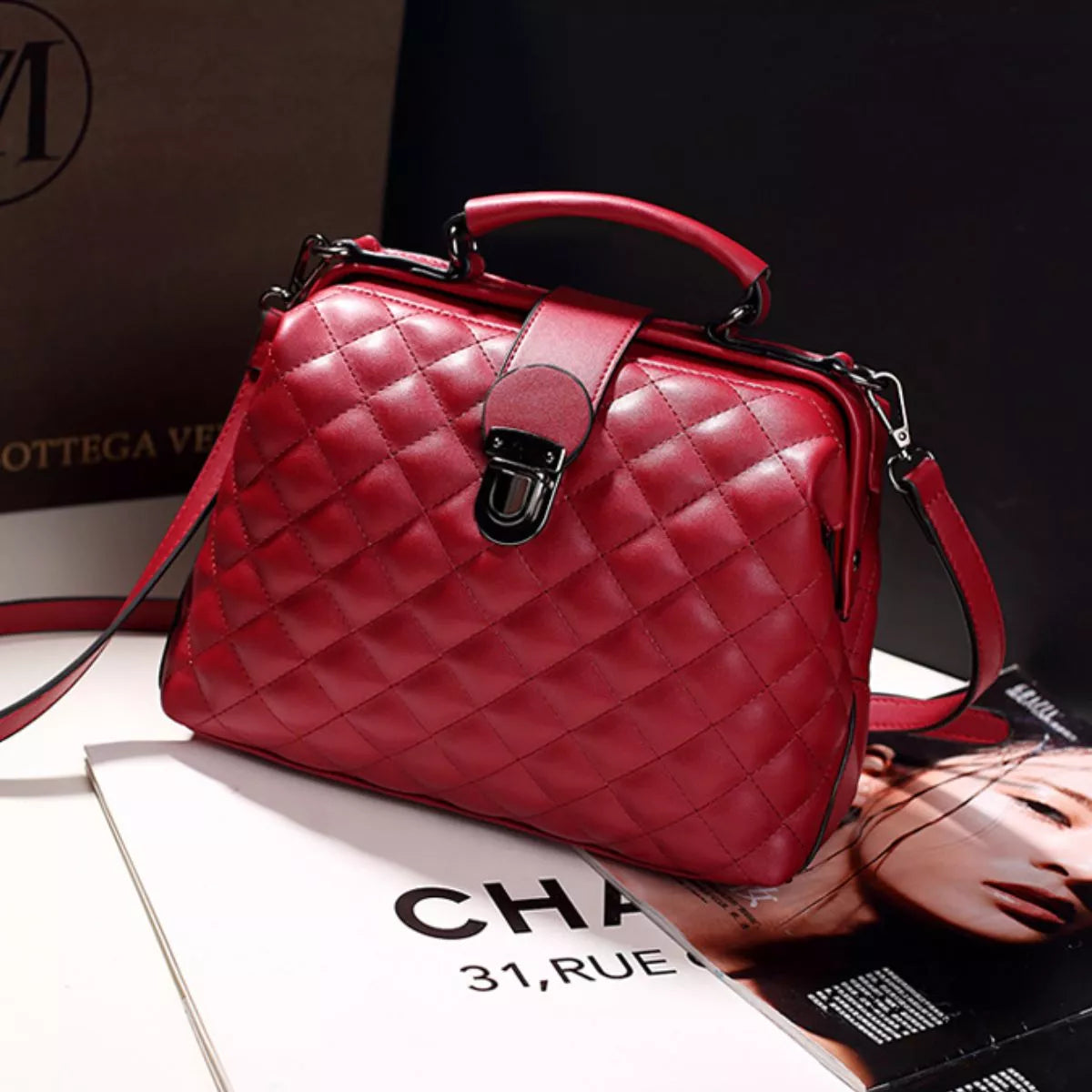 A red quilted leather handbag with a top handle, front strap closure, and shoulder strap, styled on top of a magazine with a dark background.