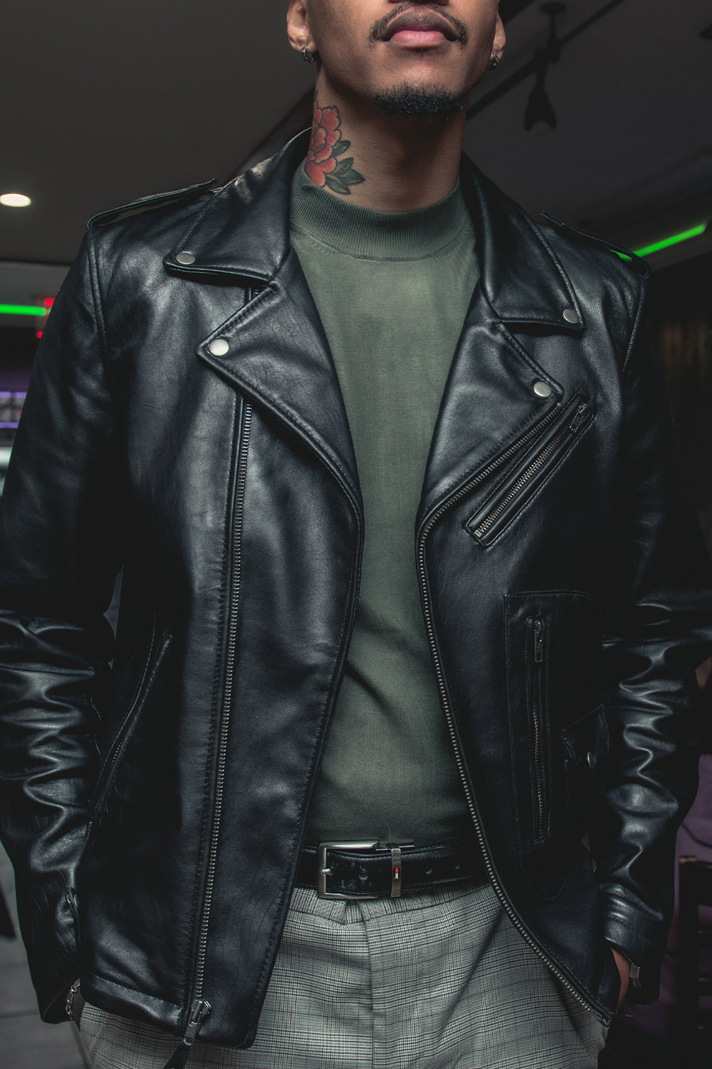 Person wearing a black leather jacket and green shirt in an indoor setting
