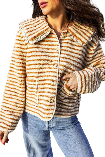 A woman wearing a fuzzy striped cropped jacket in brown and cream, paired with blue jeans, photographed outdoors on a sunny day.