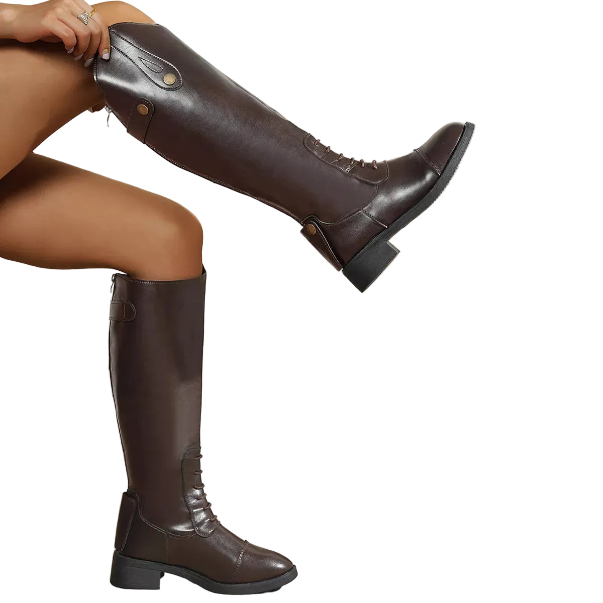 A person wearing dark brown knee-high leather boots, with one boot raised on a tiled floor against a white paneled wall. A large terracotta planter with dried pampas grass sits to the right.