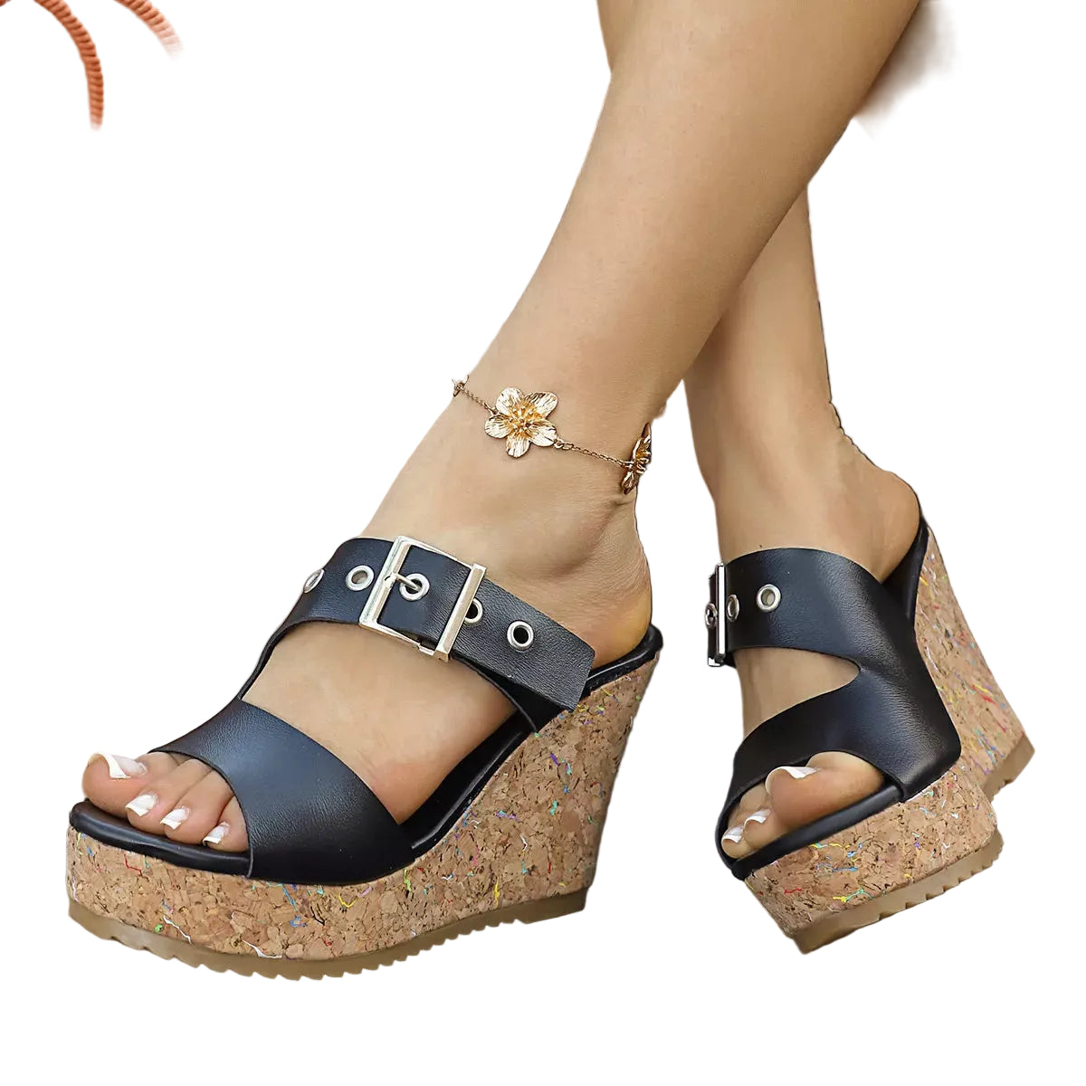 A pair of women's black wedge sandals with cork-look platform soles and silver-tone buckle straps, shown on a model's feet on a wooden deck. The model is also wearing a gold anklet, with a wicker basket of white flowers in the background.
