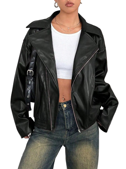 A woman wearing a black faux-leather moto jacket with silver zippers, styled over a white crop top and blue jeans.