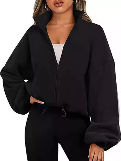 A woman wearing a black cropped zip-up jacket with oversized balloon sleeves and black jogger pants, shown against a plain white background.