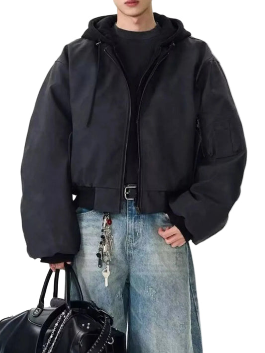 A person wearing a black oversized zip-front jacket with a hood, layered over a black top and light blue jeans, holding a black handbag against a plain light background.