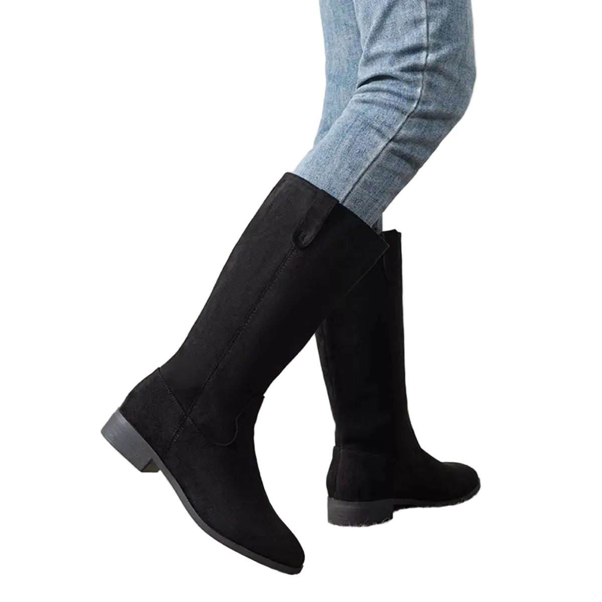 A person wearing black knee-high boots with light blue jeans, standing on a textured beige rug against a plain off-white wall.