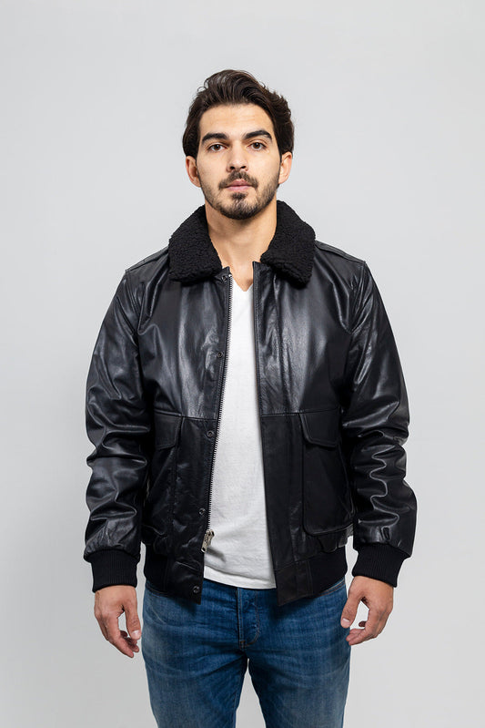 Man wearing a black leather jacket over a white shirt with blue jeans on a light gray background
