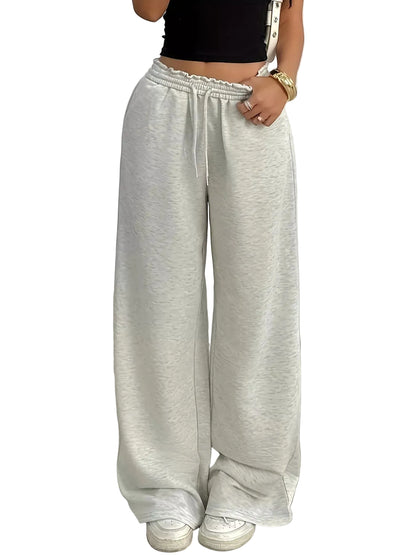 A person wearing light heather gray wide-leg sweatpants with an elastic drawstring waist, paired with a black crop top and white sneakers, standing indoors against a plain light gray wall.