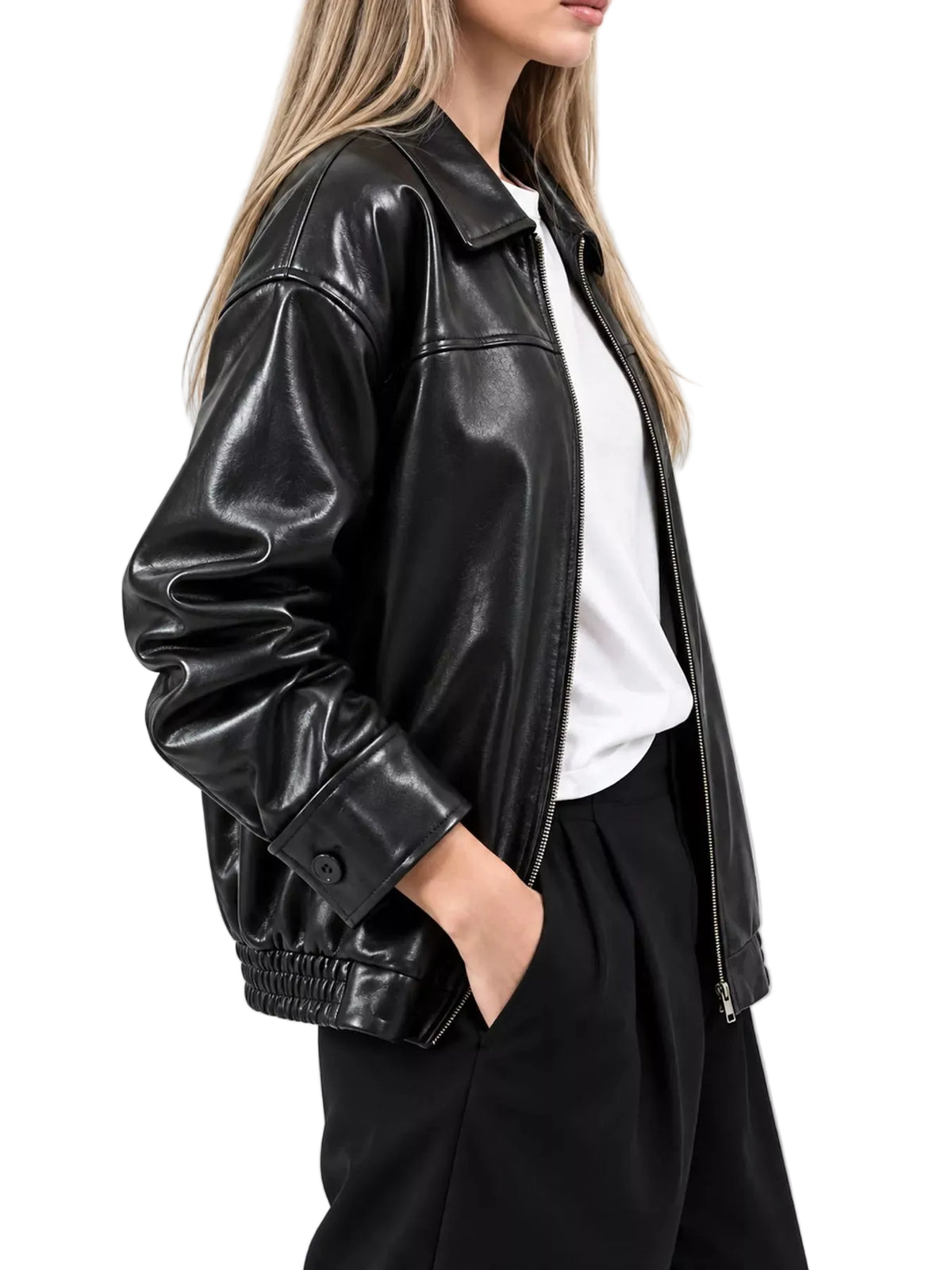 A woman wearing a black faux-leather moto jacket over a white t-shirt and black pants, shown from the side against a light gray background.
