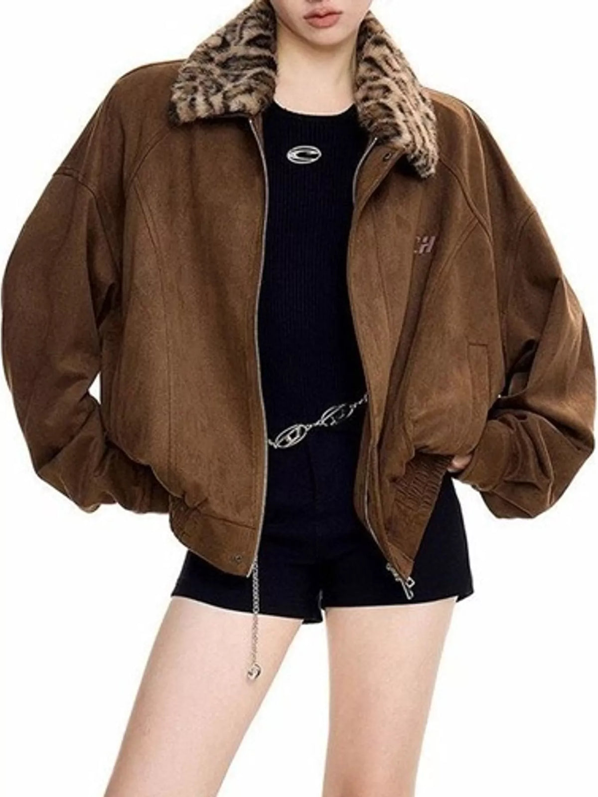 A model wearing an oversized brown suede bomber jacket with a leopard-print faux fur collar, styled over a black ribbed top and black shorts.