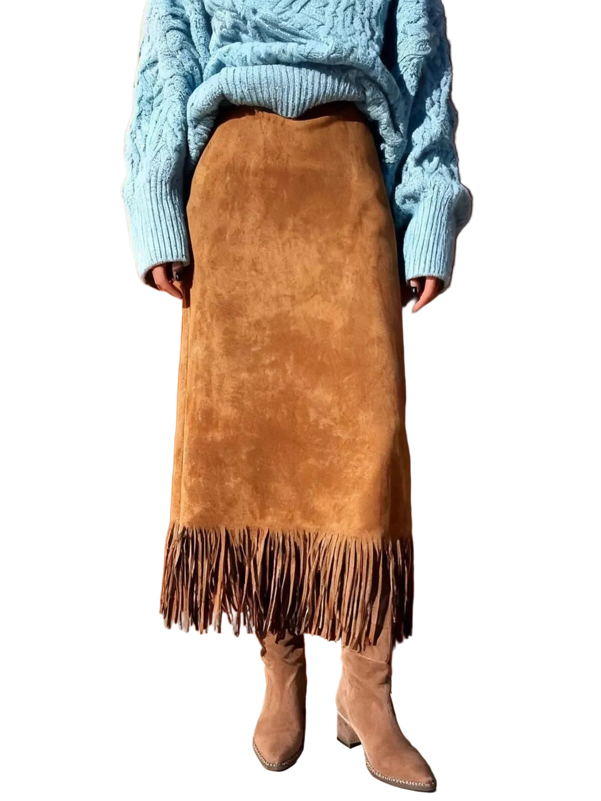 A person wearing a brown suede-like fringe skirt with a light blue cable-knit sweater and brown heeled boots, standing against a warm orange-brown wooden wall.