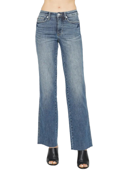 A model from the waist down wearing medium-wash blue denim jeans with a straight-to-flare leg and black open-toe heeled sandals, photographed against a plain white studio background.