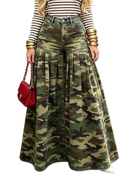 A person standing on a garden path wearing a high-waisted, wide-leg camouflage denim skirt paired with a black and white striped long-sleeve top and gold bracelets, holding a red handbag.