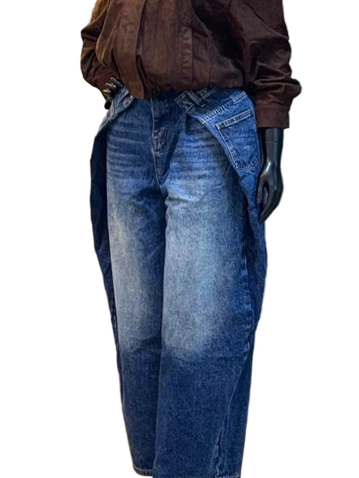 A pair of wide-leg blue denim jeans shown on a black mannequin torso, styled with a dark brown blouse. The background is a textured gray stone wall with decorative green leaves.