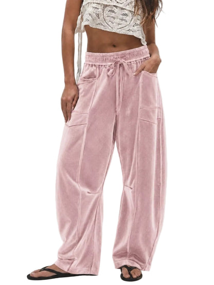 A model wearing dusty pink velvet wide-leg pants with a drawstring waist, side pockets, and front patch pockets, paired with a white crochet crop top and black flip-flops against a light gray background.