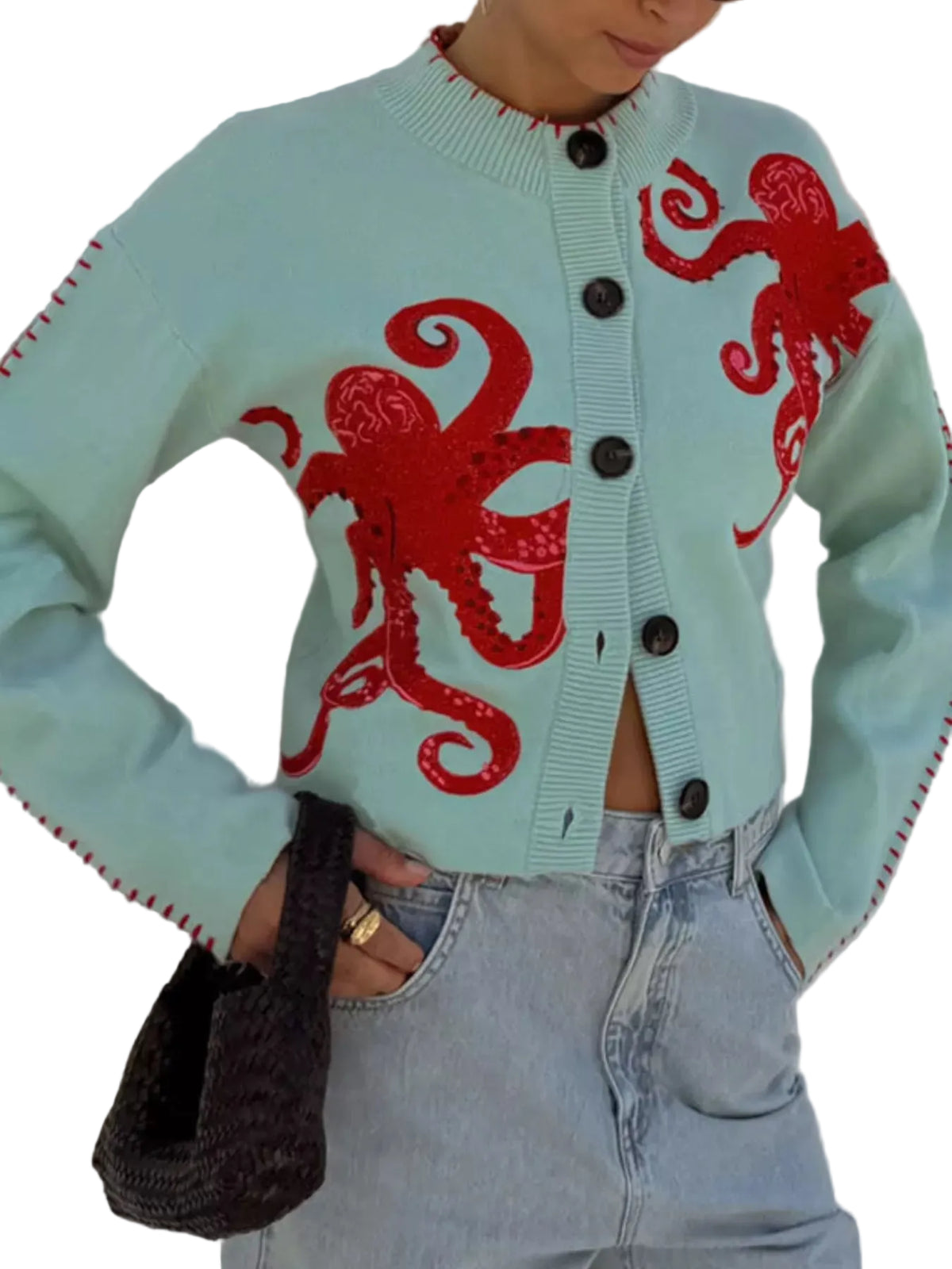 A person wearing a light mint green cropped cardigan with large red octopus embroidery and black buttons, paired with light-wash jeans and holding a dark woven bag.