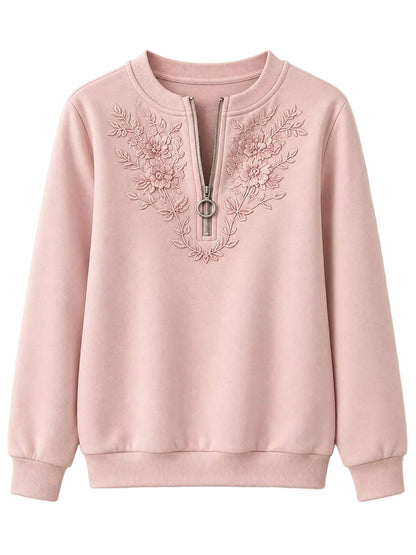 A light pink crewneck sweatshirt with a half-zip neckline, featuring delicate floral embroidery on the chest and a silver-tone zipper pull.
