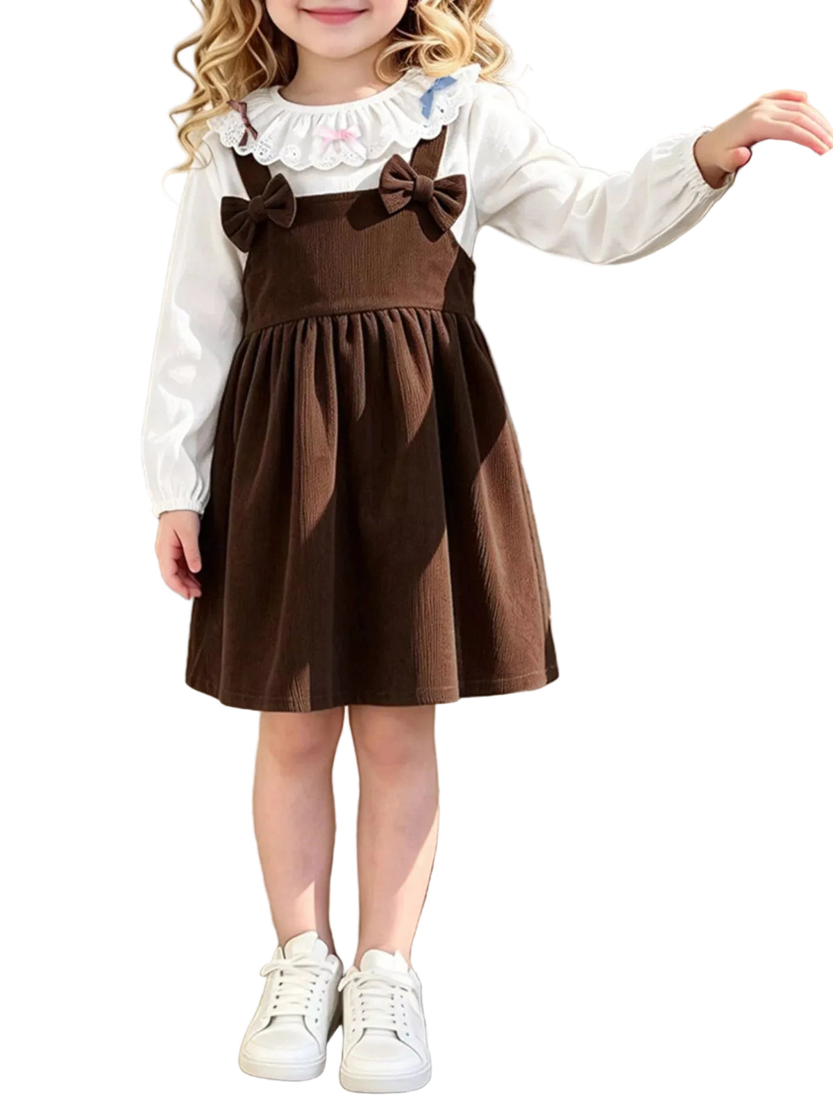A young girl wearing a brown corduroy pinafore dress with a white long-sleeve shirt underneath, standing on indoor stairs.