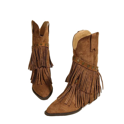 A pair of brown suede fringe cowboy boots with pointed toes and bronze-tone metal studs, displayed on a solid light beige background.