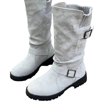 A pair of light gray suede-like mid-calf boots with black soles and silver buckle straps, shown standing on weathered wooden planks.