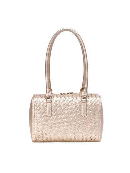 A structured woven leather handbag in a light champagne-gold color, featuring a top handle and a basketweave pattern, shown against a solid gray background.