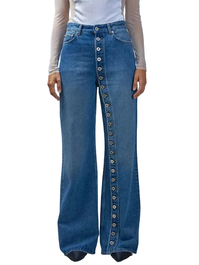 A model wearing high-waisted, wide-leg blue denim jeans featuring a prominent vertical row of decorative buttons down the front center, styled with a white ribbed long-sleeve top against a neutral gray studio background.