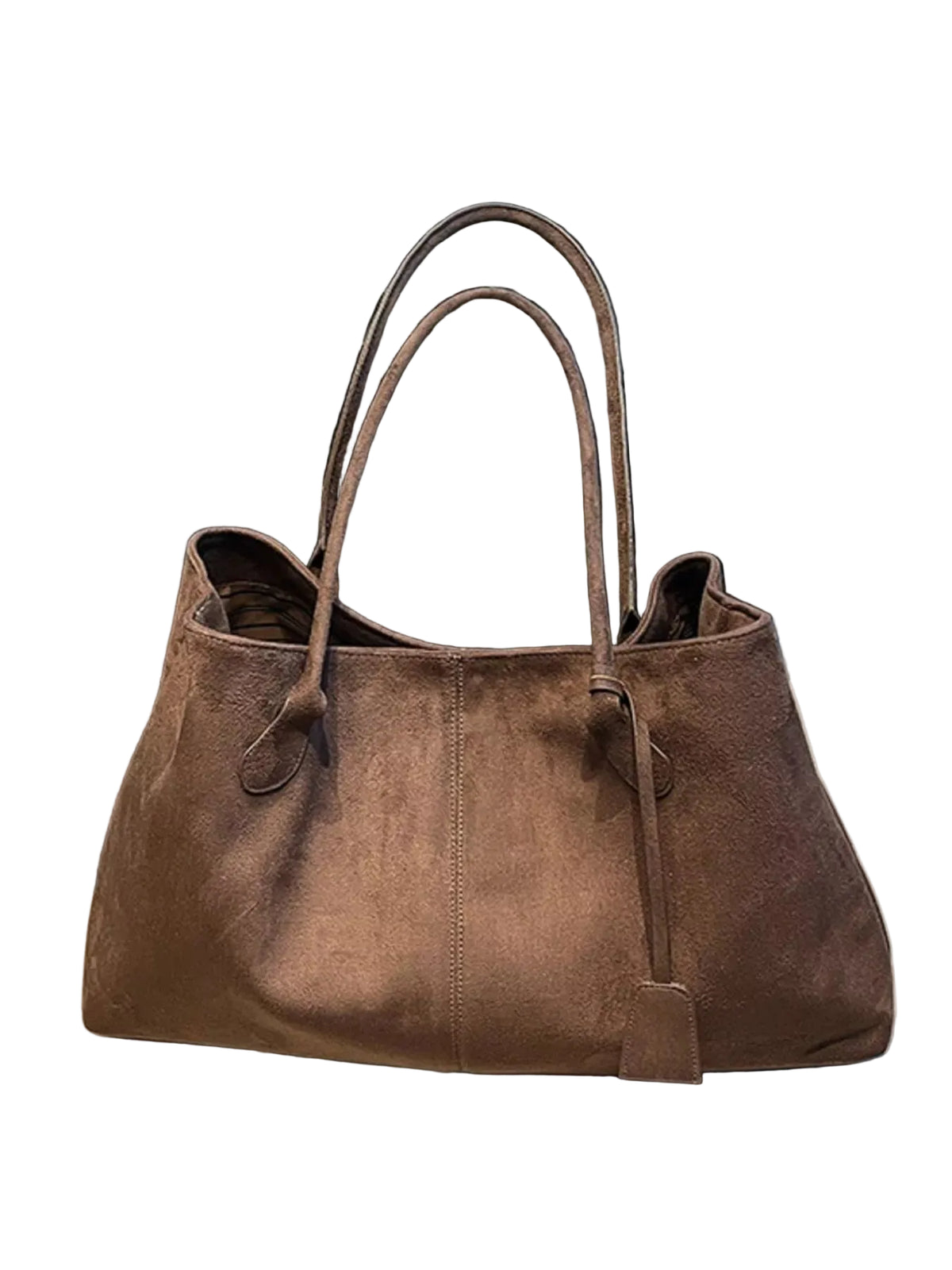A large brown suede tote bag with double shoulder straps, resting on a magazine in front of a black leather sofa.