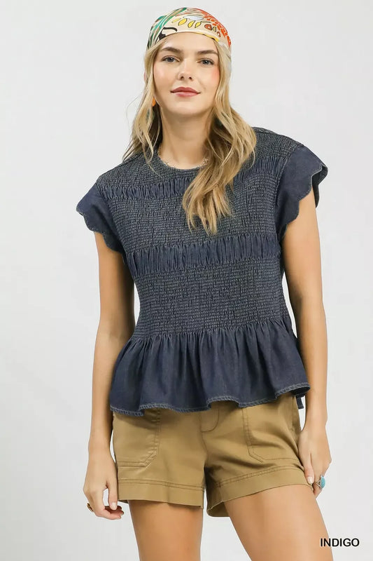 Woman wearing a dark blue peplum top and beige shorts with a colorful headband on a light gray background.