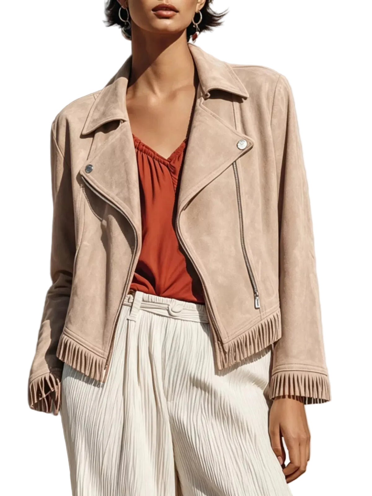 A woman models a beige suede moto jacket with fringe details, worn over a rust-orange top and white pleated trousers, set against a textured concrete wall with strong sunlight and shadows.