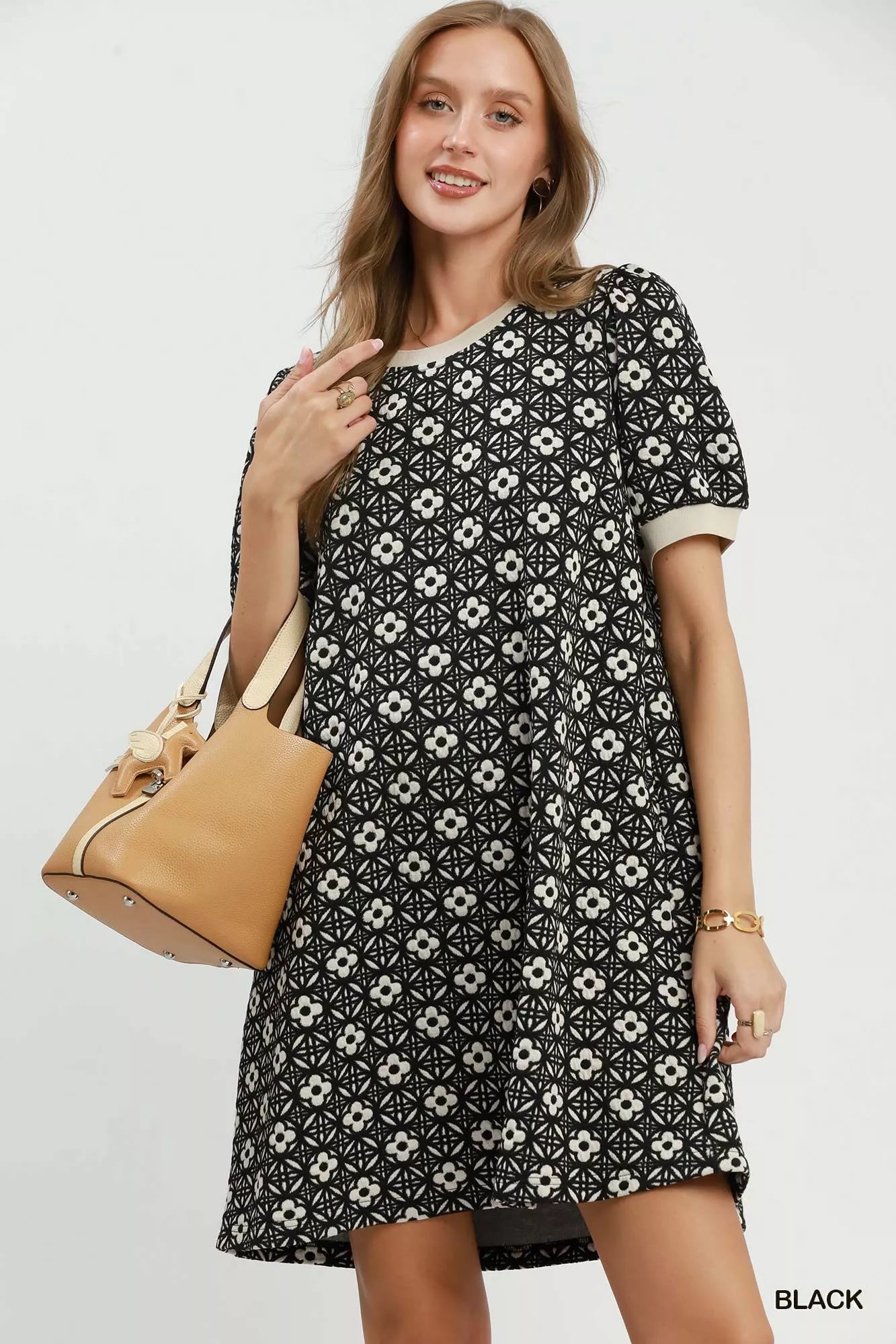 Woman wearing a black floral dress holding a beige handbag on a white background