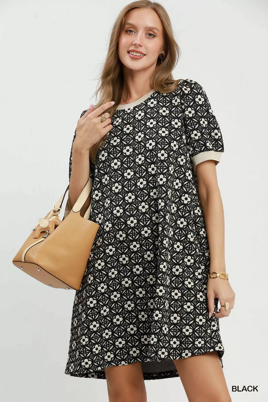 Woman wearing a black floral dress holding a beige handbag on a white background