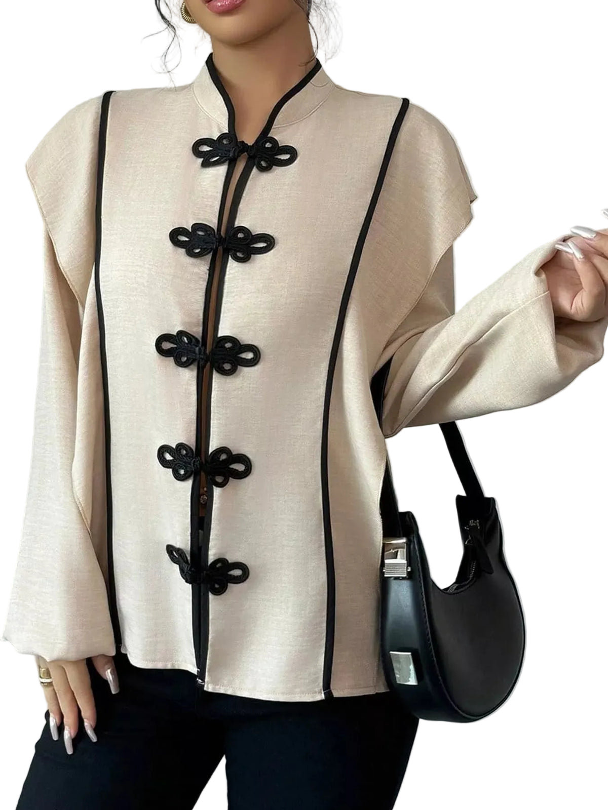 A woman wearing a beige long-sleeve blouse with black trim and decorative black front buttons, paired with black pants and carrying a black handbag against a plain light gray background.