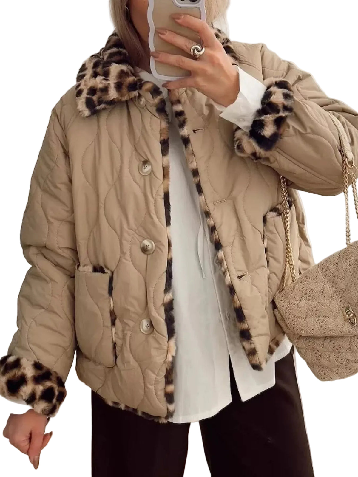 A person wearing a beige quilted puffer jacket with leopard-print faux fur trim on the collar, cuffs, and front opening, layered over a white top and dark pants, while holding a phone in a mirror selfie. A matching beige textured handbag is also visible.
