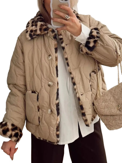 A person wearing a beige quilted puffer jacket with leopard-print faux fur trim on the collar, cuffs, and front opening, layered over a white top and dark pants, while holding a phone in a mirror selfie. A matching beige textured handbag is also visible.