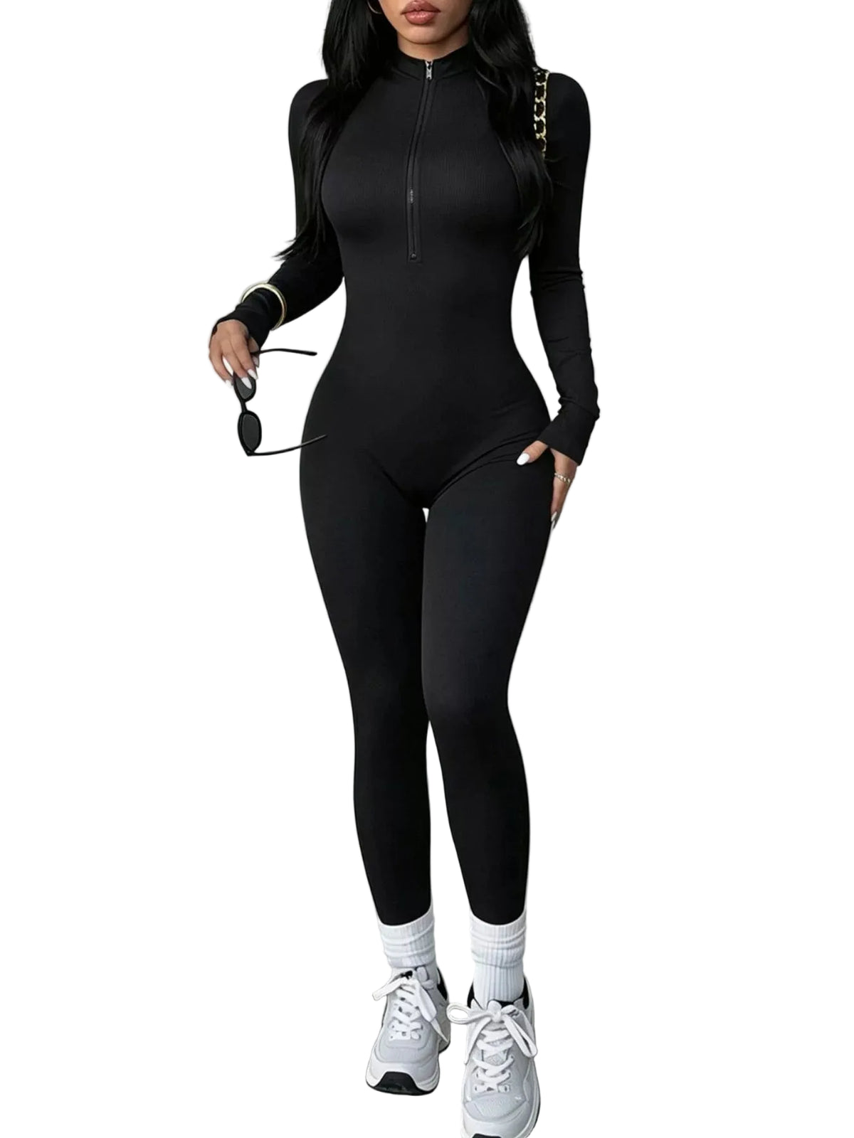 A woman modeling a black long-sleeve zip-up bodysuit with matching leggings, styled with white socks and white sneakers, standing outdoors next to a white wall.