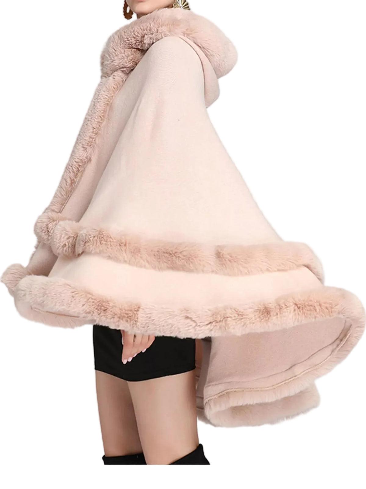 A woman wearing a light blush pink hooded cape with plush faux-fur trim, shown against a plain light gray studio background.
