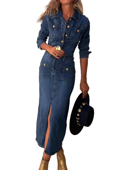 A woman models a blue denim shirt dress with gold buttons, holding a black studded hat, standing next to a white surfboard against a beige wall.