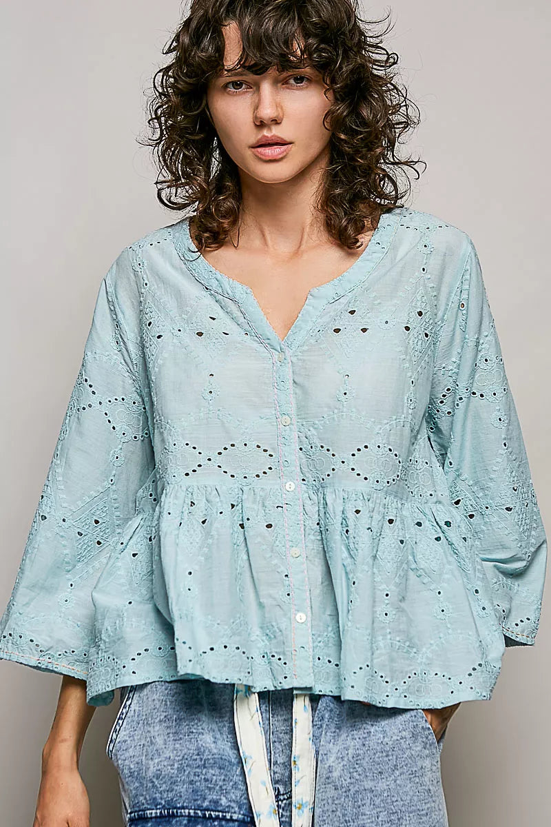 Woman wearing a light blue blouse with intricate patterns against a plain background