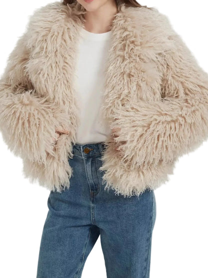 A person wearing a shaggy, long-pile faux fur jacket in a light beige color, styled over a white t-shirt and blue jeans against a plain white background.